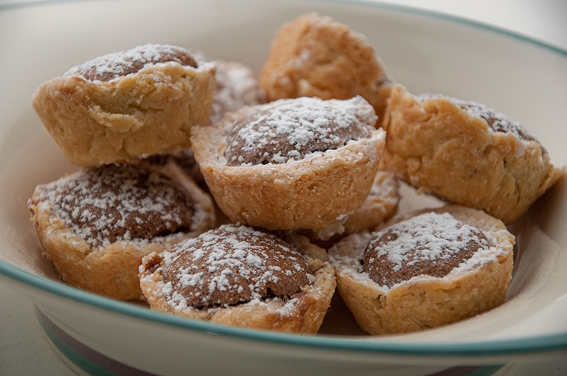 Bowl with several pecan tassies covered in powdered sugar.