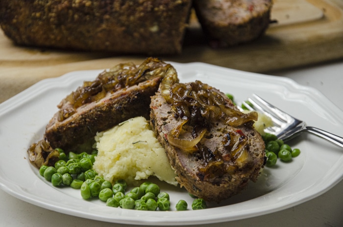 grilled meatloaf on plate with potatoes and peas.