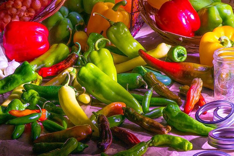 Assorted peppers next to empty glass jars.