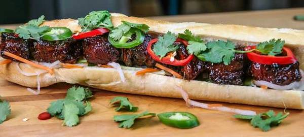Baguette, split and filled with meat, red and green jalapenos, and garnished with cilantro