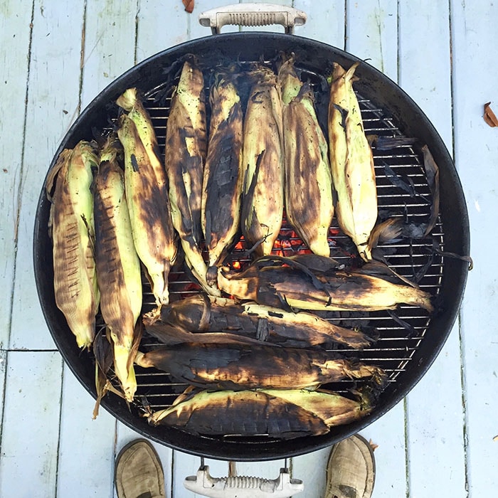 charred corn in husks on charcoal grill