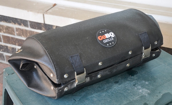 Black leathery cylindrical shaped bag with two shiny buckles to snap it shut.