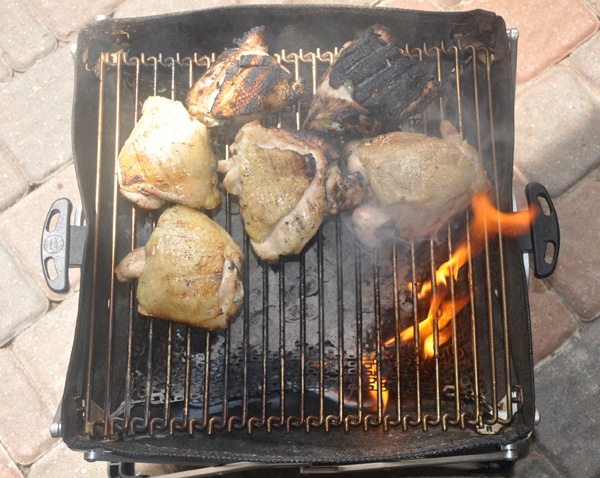 Chicken thighs on a small grill. There is a grease fire and some thighs are burnt.