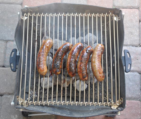Five sausages cooking on a small BBQ grill.