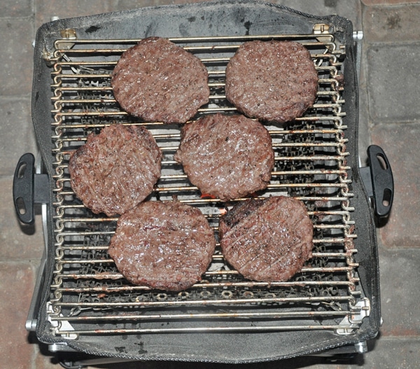 Six hamburgers finished cooking on a small grill.