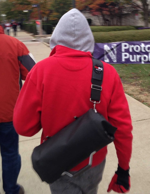 Person with red jacket walking with a black roll up bag slung over the shoulder.