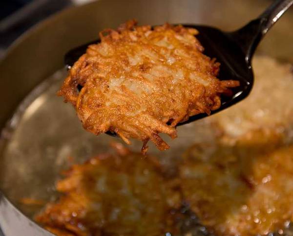 A crispy potato latke lifted from the oil on a slotted spoon
