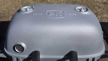 Shiny hood of grill with round dials on each side. "PK" is embossed on the top. 