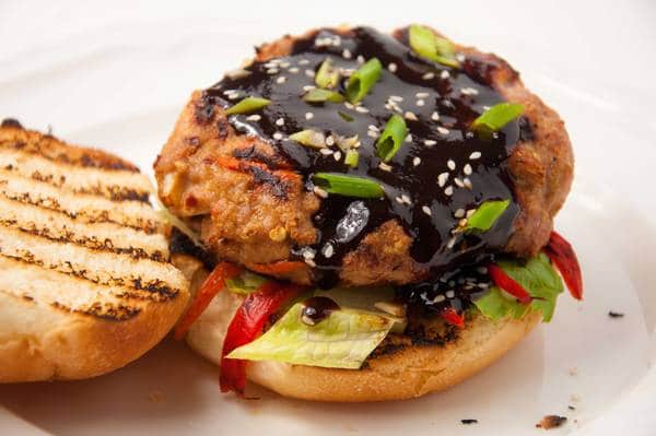 Burger covered in sauce, sitting on a bun with lettuce and tomato