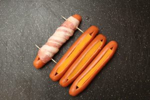 Cheese stuffed hot dogs being wrapped in bacon