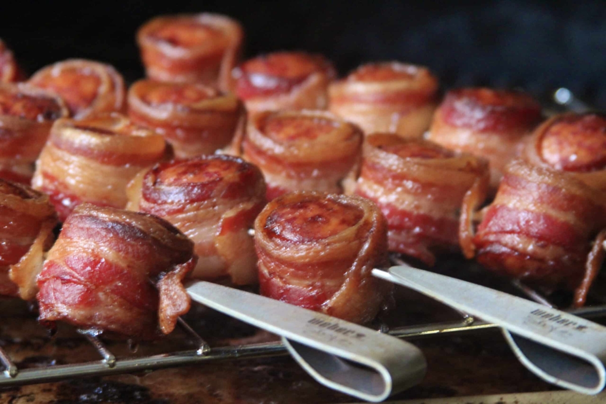 bacon wrapped kielbasa on a grill.