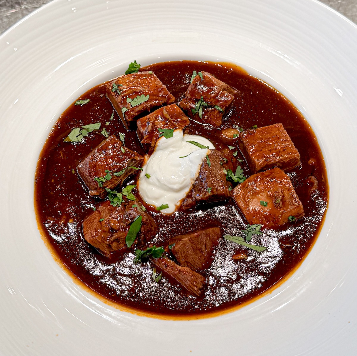pozole rojo in a white bowl garnished with sour cream and cilantro.