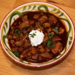 pozole rojo in a decorative bowl garnished with sour cream and cilantro.