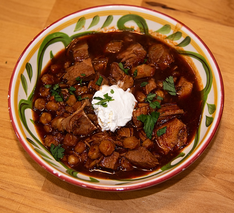 pozole rojo in a decorative bowl garnished with sour cream and cilantro.