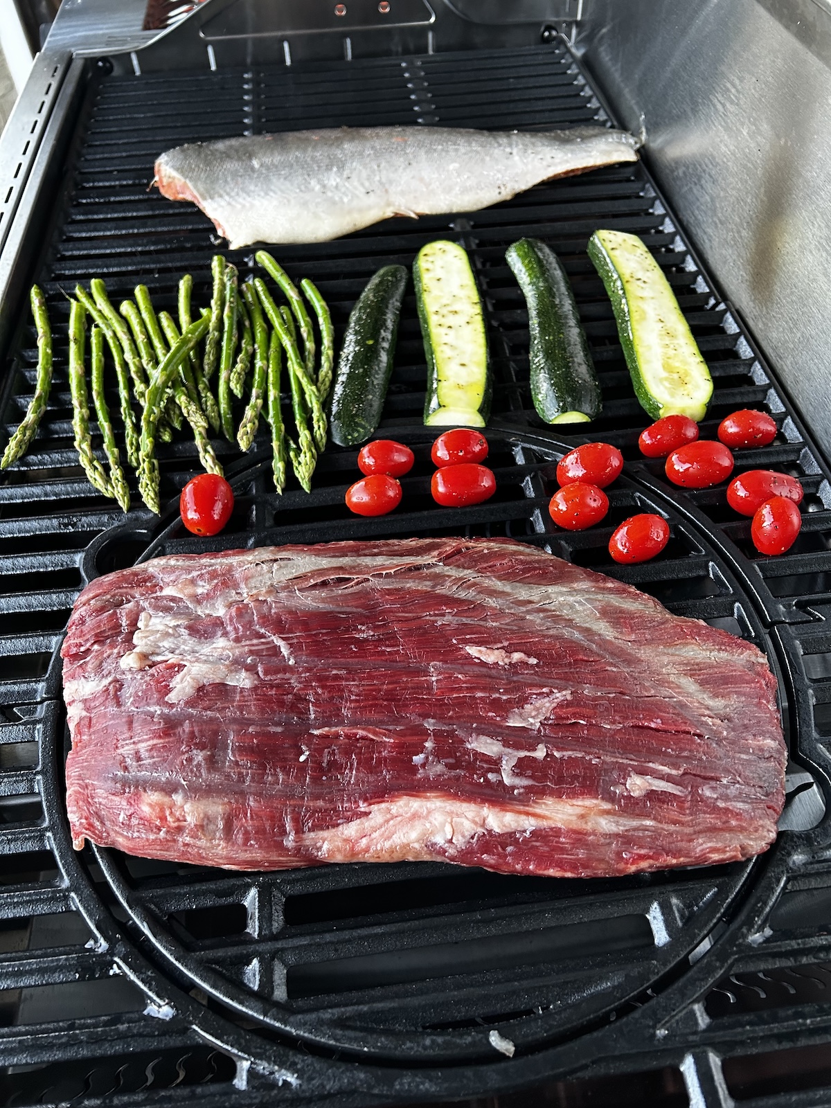 flank steak, salmon, asparagus, zucchini and cherry tomatoes on grill.