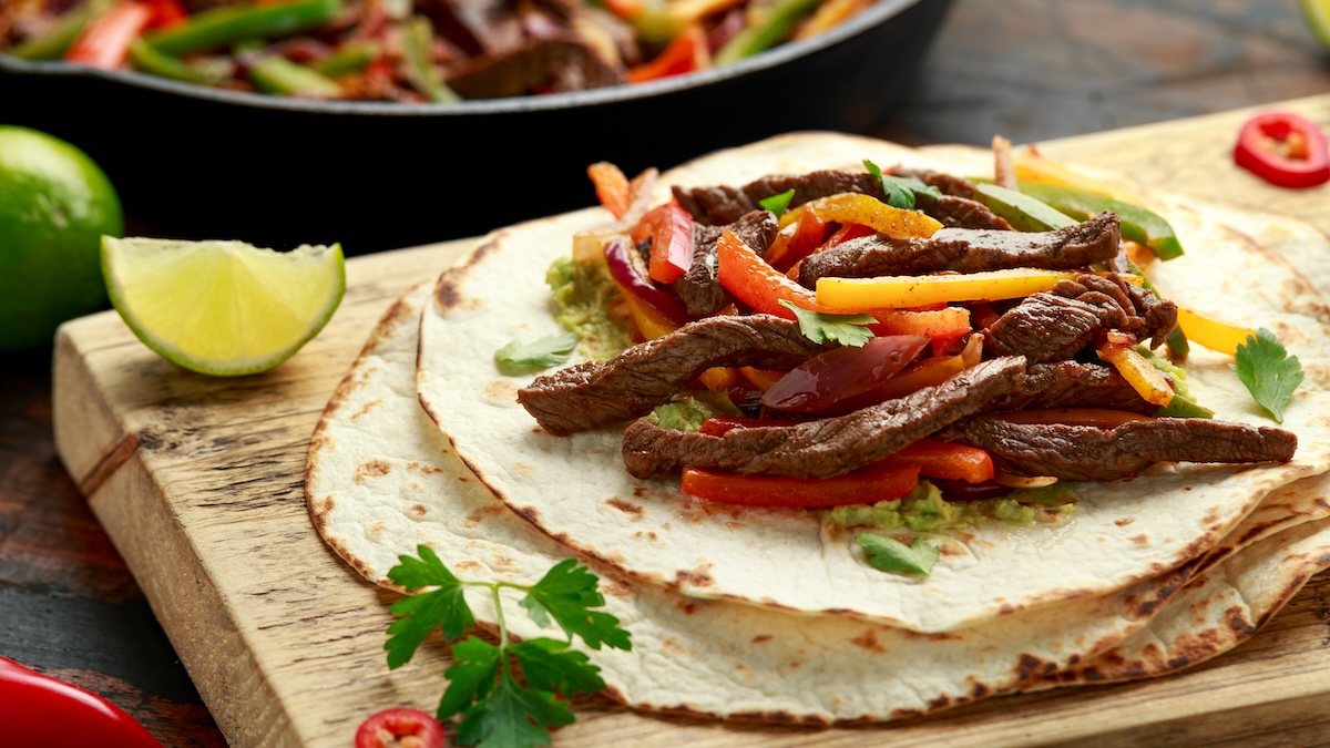 Breeo steak fajitas assembled on tortillas on a wooden board