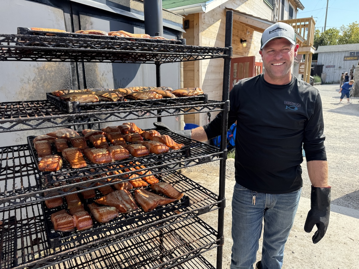 Mike Burda from Carlsons Fish and Smokehouse standing  next to a rack of smoked fish.