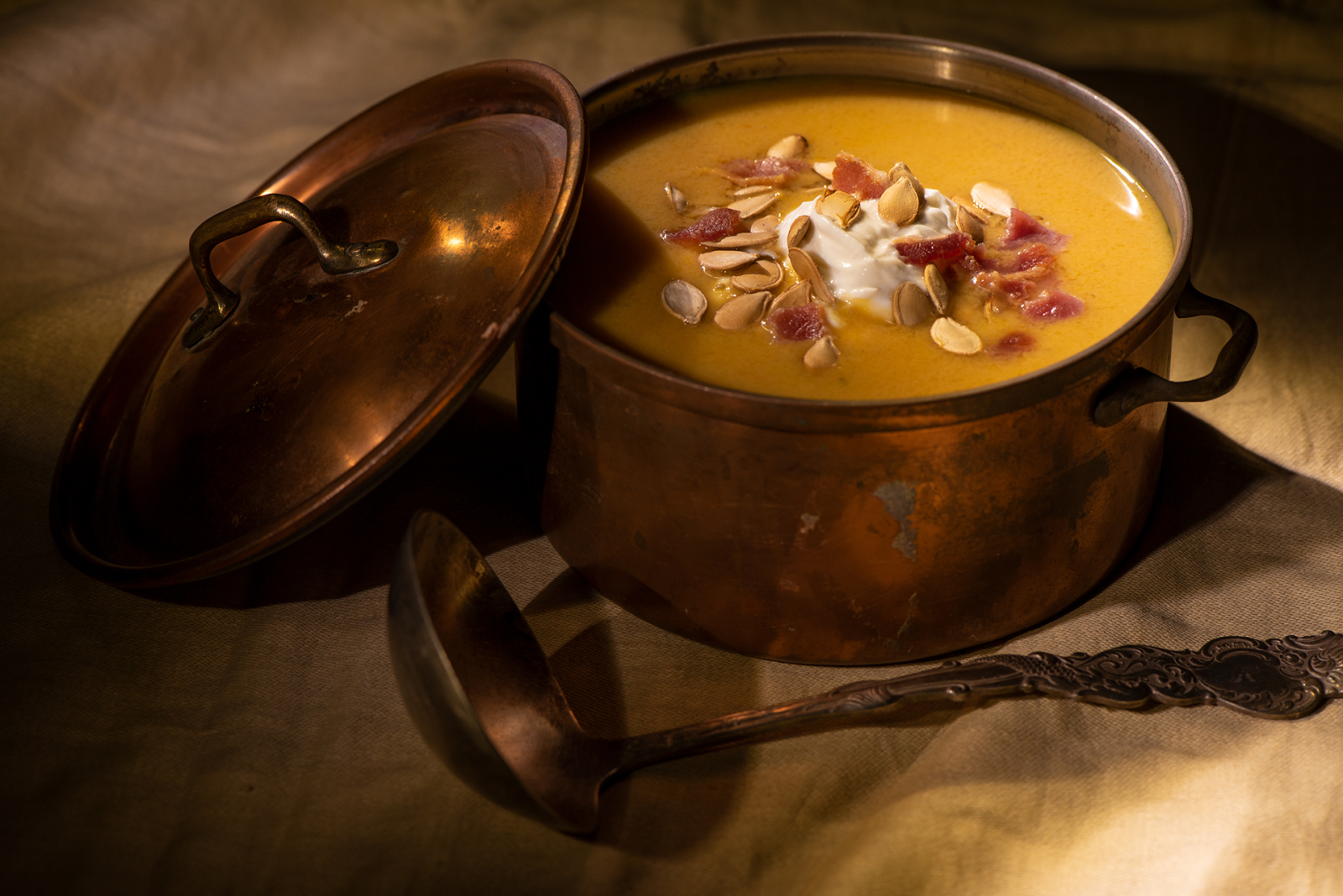 smoked squash bisque in a copper pot on a table with a ladle.